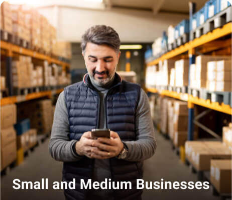 Man using a smartphone in a warehouse with shelves of boxes.